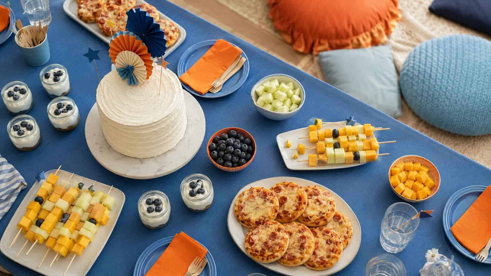 Mesa de cumpleaños temática Bluey con paleta azul y naranja — mini pizzas, brochetas de fruta y tarta sencilla