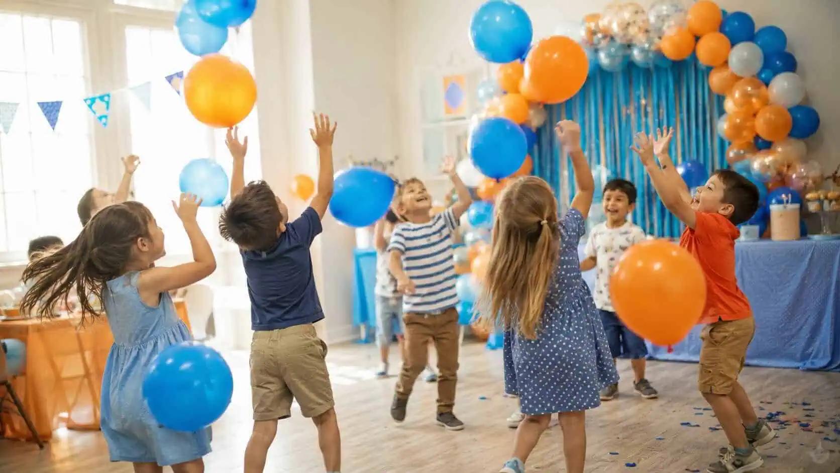 Niños jugando a Keepy Uppy con globos azules y naranjas en una fiesta de cumpleaños infantil